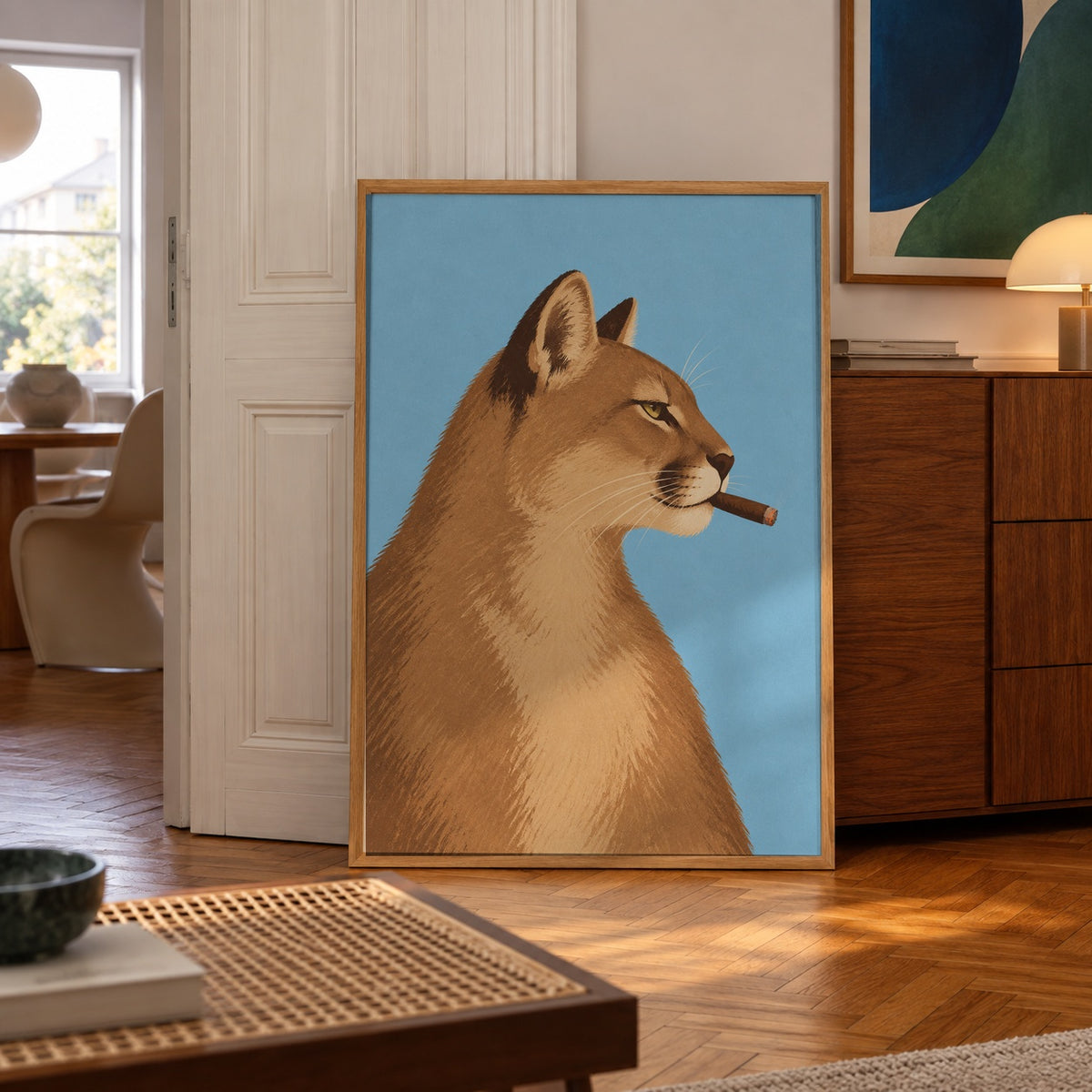 A sly mountain lion strikes a confident pose, cigar in mouth, against a bold sky-blue backdrop — poster displayed in a styled room