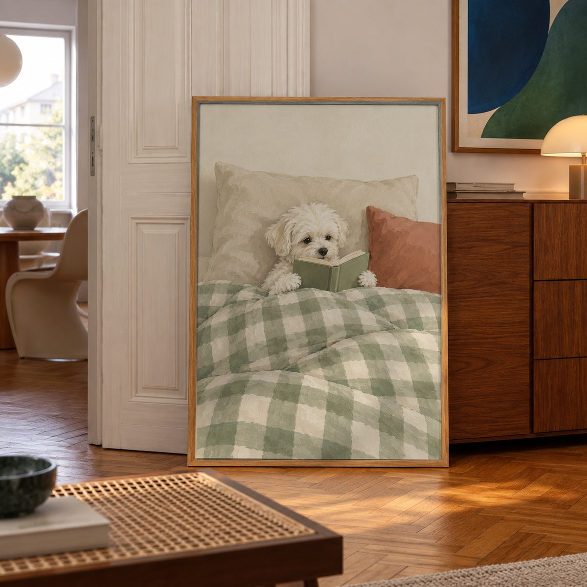 A fluffy white puppy curls up in bed, nose in a little green book — poster displayed in a styled room