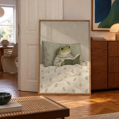 A whimsical frog in striped pajamas enjoys a quiet morning in bed, book in paw and cocoa close by — poster displayed in a styled room