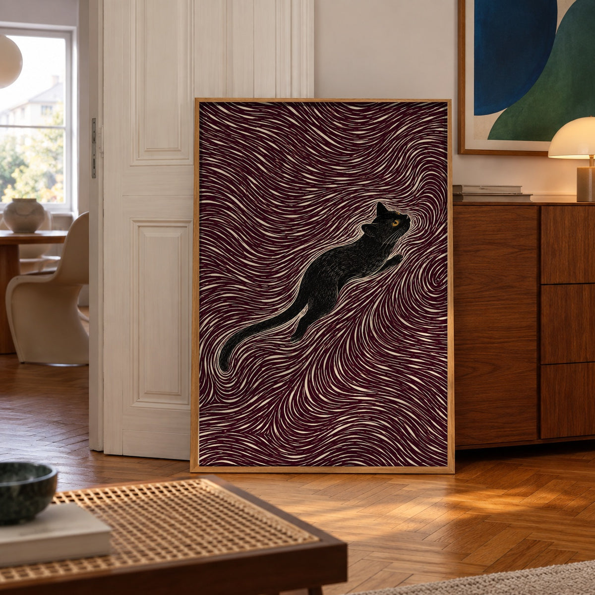 A sleek black cat stretches gracefully through a hypnotic swirl of maroon and cream lines — poster displayed in a styled room